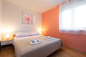 Une chambre à coucher avec un lit, deux tables de chevet avec des lampes, un grand tableau floral accroché au mur et une fenêtre avec des rideaux.