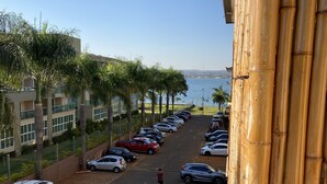Un parking avec des voitures, une personne qui marche, et une vue sur la mer et les bâtiments en arrière-plan.