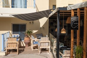 An outdoor seating area with wooden furniture, a large potted plant, and a restaurant sign.