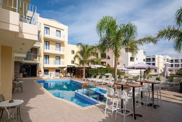 A pool area with lounge chairs, umbrellas, and a building with balconies.