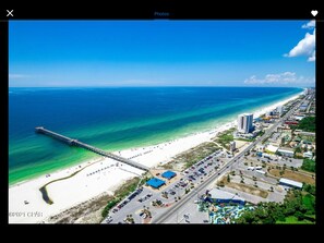 An aerial view of a coastal area with a beach, a pier, and adjacent urban development.