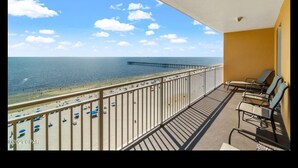 Ein Balkon mit Blick auf Strand und Steg, ausgestattet mit Liegestühlen und einer Brüstung.