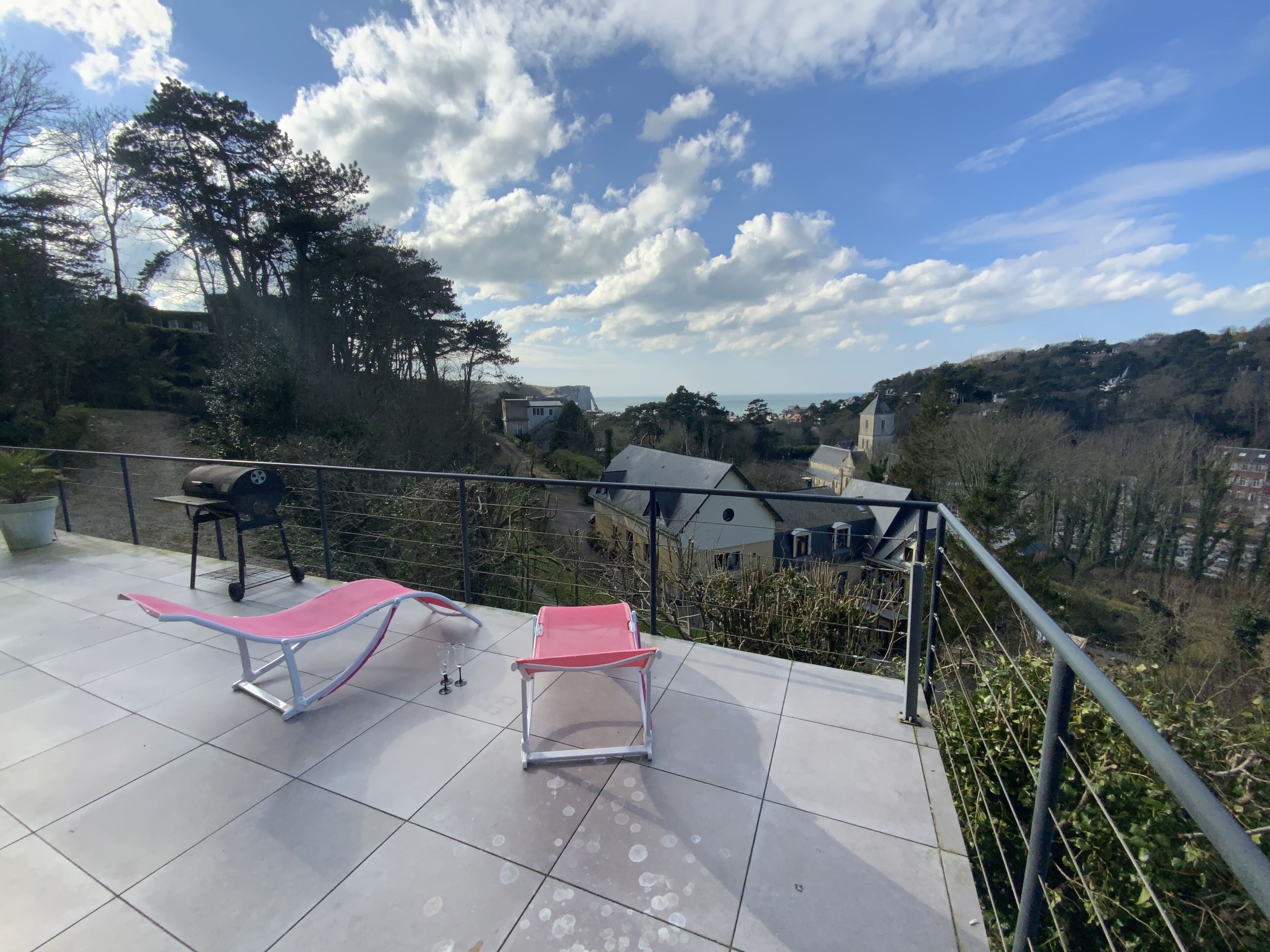 Een terras met twee loungestoelen, een barbecue en een mooi uitzicht op huizen en heuvels.