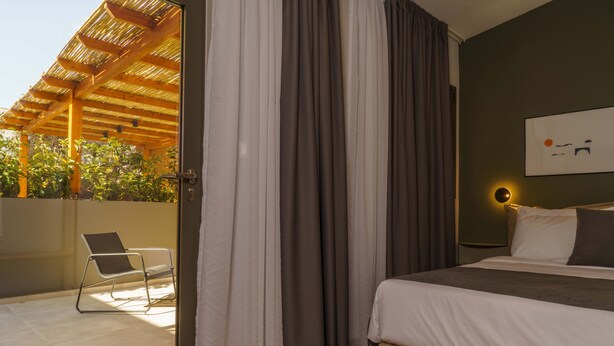 Une chambre avec un lit, une chaise et une vue sur un espace extérieur agrémenté d’une pergola.