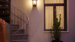 Un escalier en colimaçon, avec un pot de fleurs placé près d’une fenêtre ornée de rideaux.