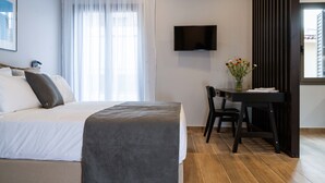 Une chambre d’hôtel moderne dotée d’un grand lit, d’un bureau avec une chaise, d’une télévision à écran plat et d’une fenêtre avec des rideaux légers.