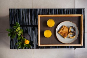 Una bandeja con un plato de comida, dos vasos de jugo de naranja y una planta con hojas verdes y una flor amarilla.