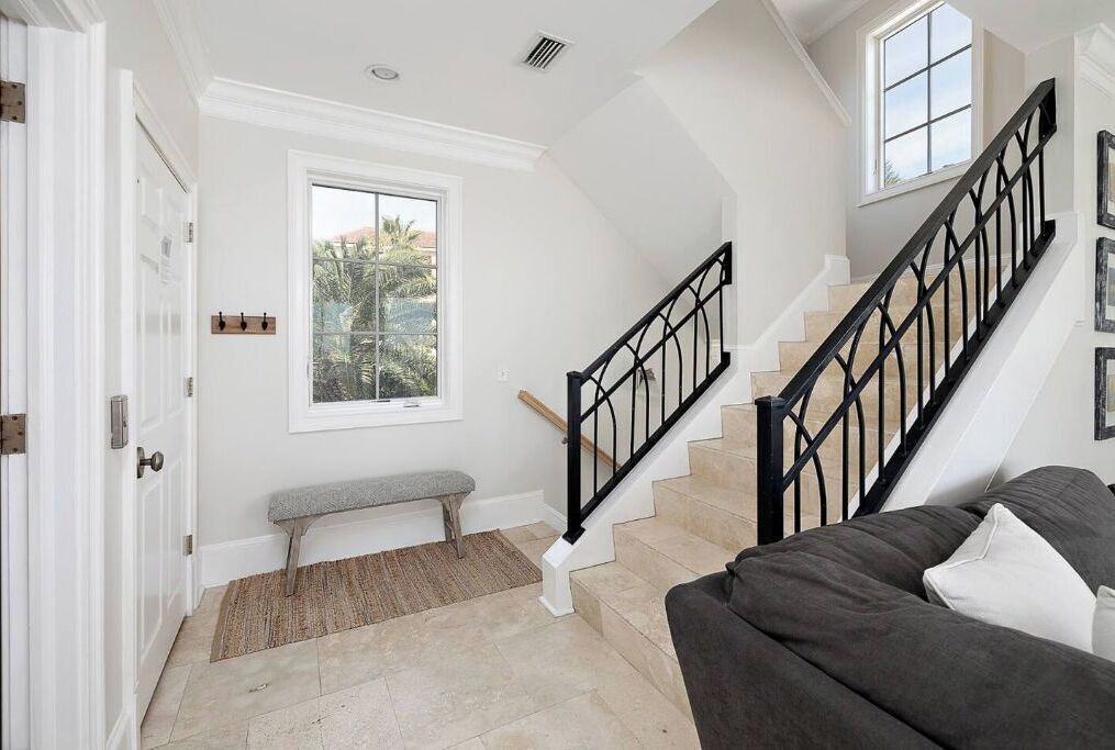 A spacious living area with a staircase, a bench, and a large window offering a view of greenery.