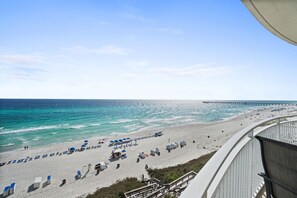 Ein Strand mit Reihen von Liegestühlen und Sonnenschirmen, ein Steg, der sich ins Meer erstreckt, und eine Treppe, die zum Strand führt.