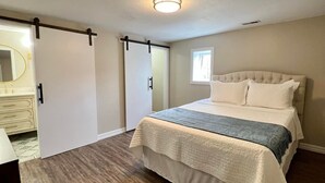 Ein Schlafzimmer mit Bett, Kommode, Tür und Deckenleuchte.