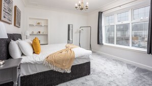 A bedroom with a bed, bedside table, lamp, and a window with curtains. - Wellington View - Donnini Apartments (Ayr)