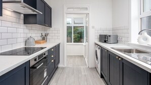 A modern kitchen with dark cabinets, white countertops, a built-in oven, a microwave, and a sink. - Wellington View - Donnini Apartments (Ayr)