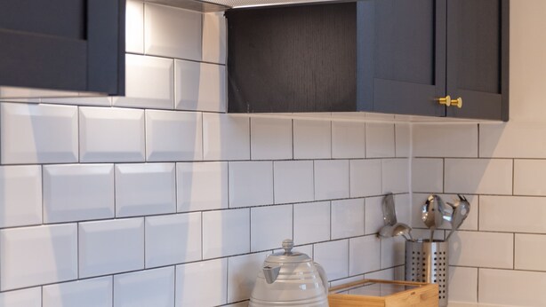 A modern kitchen with dark cabinets, white tiles, a black induction cooktop, and wooden drawers. - Wellington View - Donnini Apartments (Ayr)