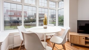 A modern room with a round table, white chairs, a TV, and large windows offering a view of the outside. - Wellington View - Donnini Apartments (Ayr)
