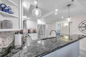 A modern kitchen with a marble countertop, stainless steel appliances, and pendant lighting.