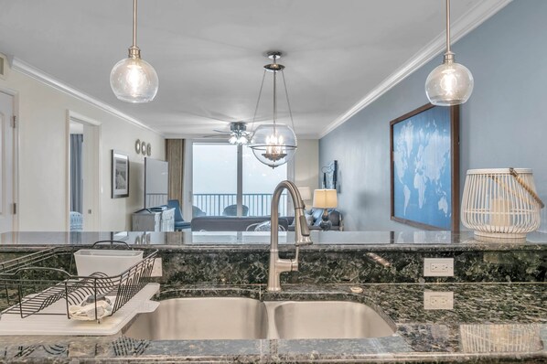 A modern kitchen with a granite countertop, stainless steel sink, and pendant lighting.