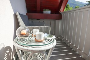 Un petit espace extérieur aménagé avec une table en verre, deux tasses blanches et un bol décoratif en verre contenant une bougie.