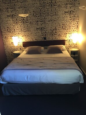 A bed with a headboard, two bedside tables, and wall-mounted lamps.