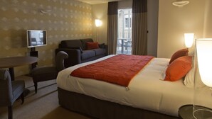 A hotel room with a large bed, a desk, a chair, a TV, and a window with curtains. - L Adresse (Saint-Malo)