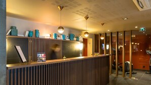 A reception area with a wooden reception desk, a menu stand, and decorative items. There are two pendant lights above the desk. - L Adresse (Saint-Malo)