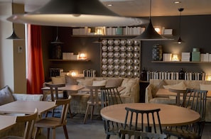 A cozy restaurant with round tables and chairs, a wall of mirrors, and shelves with books and decorative items.