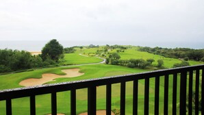 A golf course with a view of the ocean and a wooden balcony railing. - The Rich Prada Bali (Pecatu)