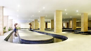 A spacious indoor pool area with multiple seating areas and a central water feature. - The Rich Prada Bali (Pecatu)
