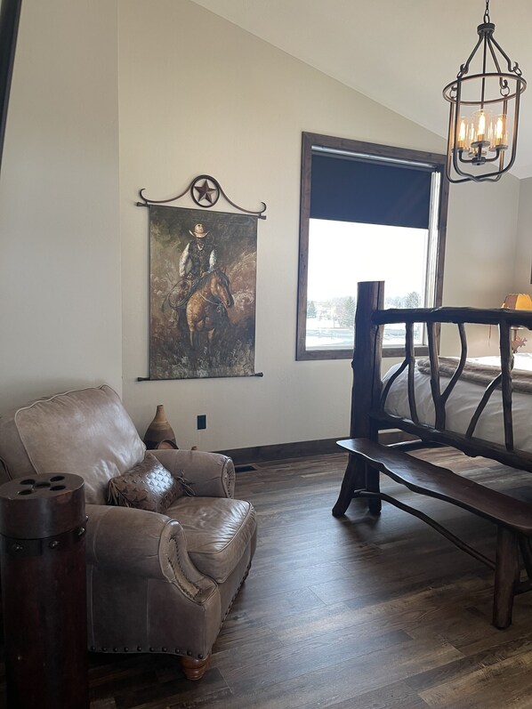 Een woonkamer met een leren bank, een houten bankje, een groot raam en een schilderij aan de muur.