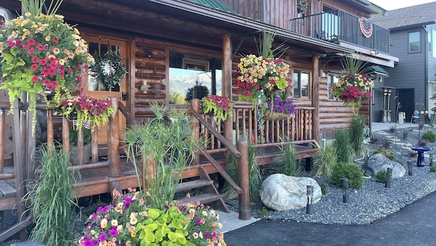 Eine Holzblockhütte mit Veranda, verziert mit hängenden Blumenkörben und Topfpflanzen.