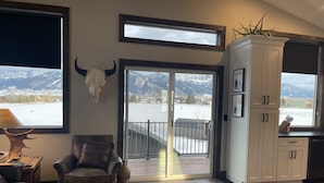 Ein Wohnzimmer mit Ledersofa, Couchtisch, aufgehängtem Kuhschädel und großem Fenster mit Bergblick.