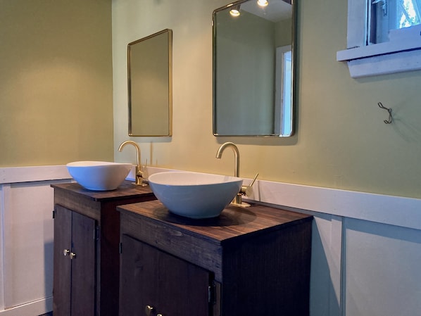 A bathroom with two sinks, each with a large bowl and a single faucet. There are two mirrors above the sinks, and a cabinet below them. - Restored 1930's Farm House (Geneva)