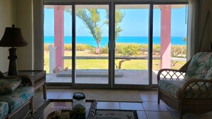 Habitación con vistas al océano a través de amplios ventanales, mobiliario de mimbre y una lámpara.