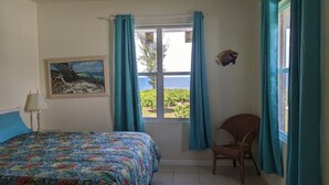 Un dormitorio con una cama, una silla, un cuadro y un ventanal con cortinas.