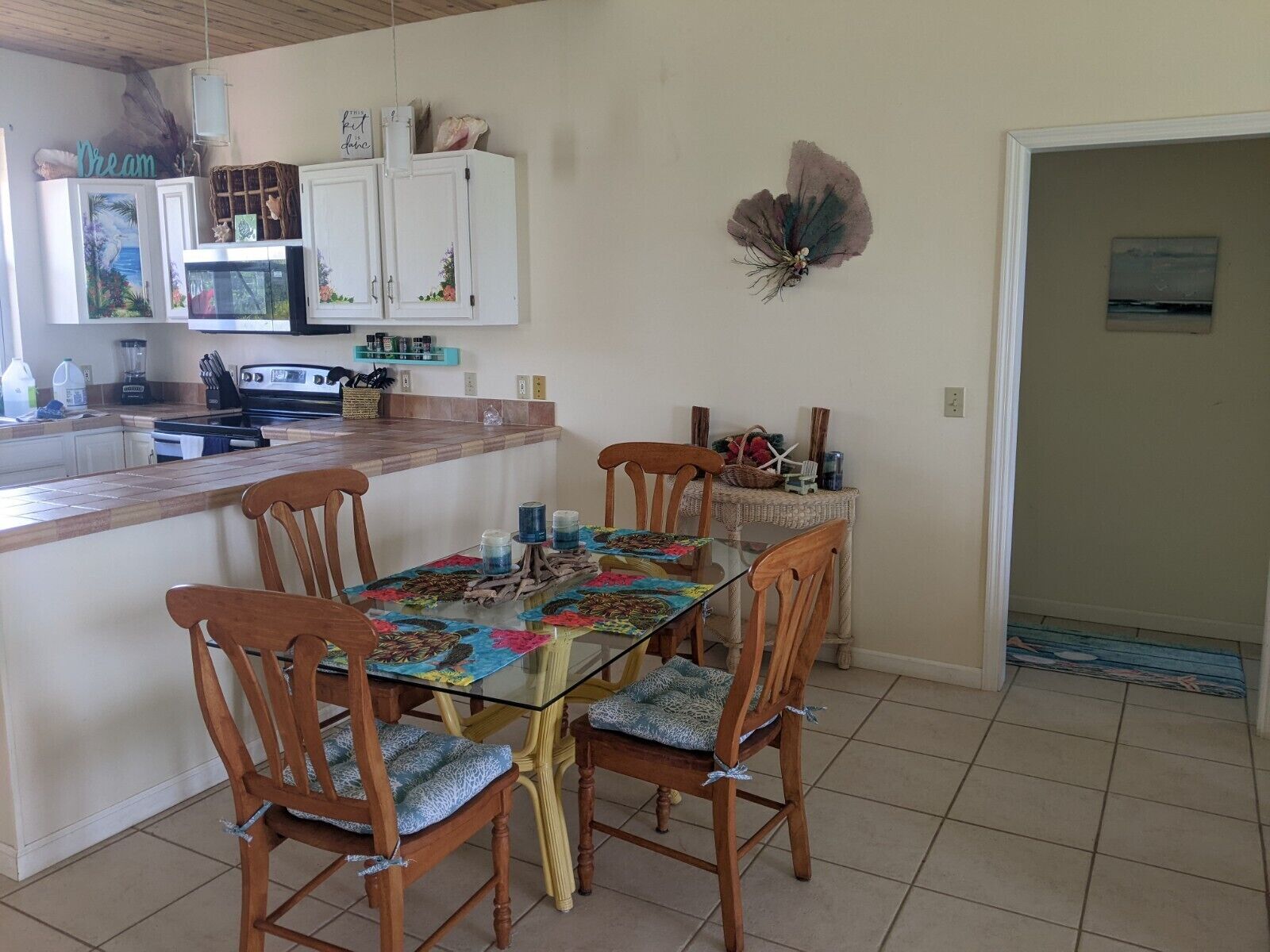 Un coin repas avec une table en verre, des chaises en bois et une cuisine en arrière-plan.