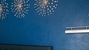 A bedroom with a dark blue wall, a bed with white bedding, a small bedside table with a vase of white flowers, and decorative wall art. - Sophisticated Haus- Houston Near NRG Stadium (Houston)