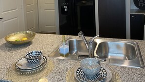 A modern kitchen with a stainless steel sink, black refrigerator, and granite countertops. - Sophisticated Haus- Houston Near NRG Stadium (Houston)