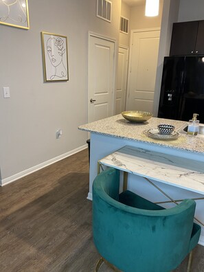 A kitchen with a marble countertop, a teal chair, and a black refrigerator.