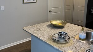 A kitchen with granite countertops, a gold bowl, a black and white patterned bowl, and a bottle of soap. - Sophisticated Haus- Houston Near NRG Stadium (Houston)