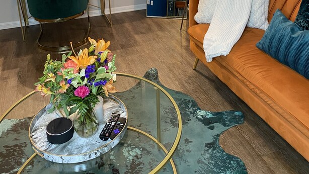 A modern living room with a glass coffee table, a sofa, a green chair, and a kitchen area in the background. - Sophisticated Haus- Houston Near NRG Stadium (Houston)