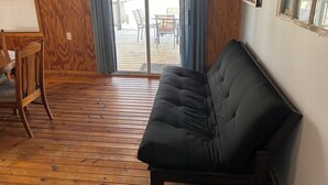 A cabin interior with a wooden floor, a black sofa, a dining table with chairs, and a sign with cabin rules.