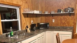 A kitchen with white cabinets, a granite countertop, a microwave, a sink, and a dining table with a chair.