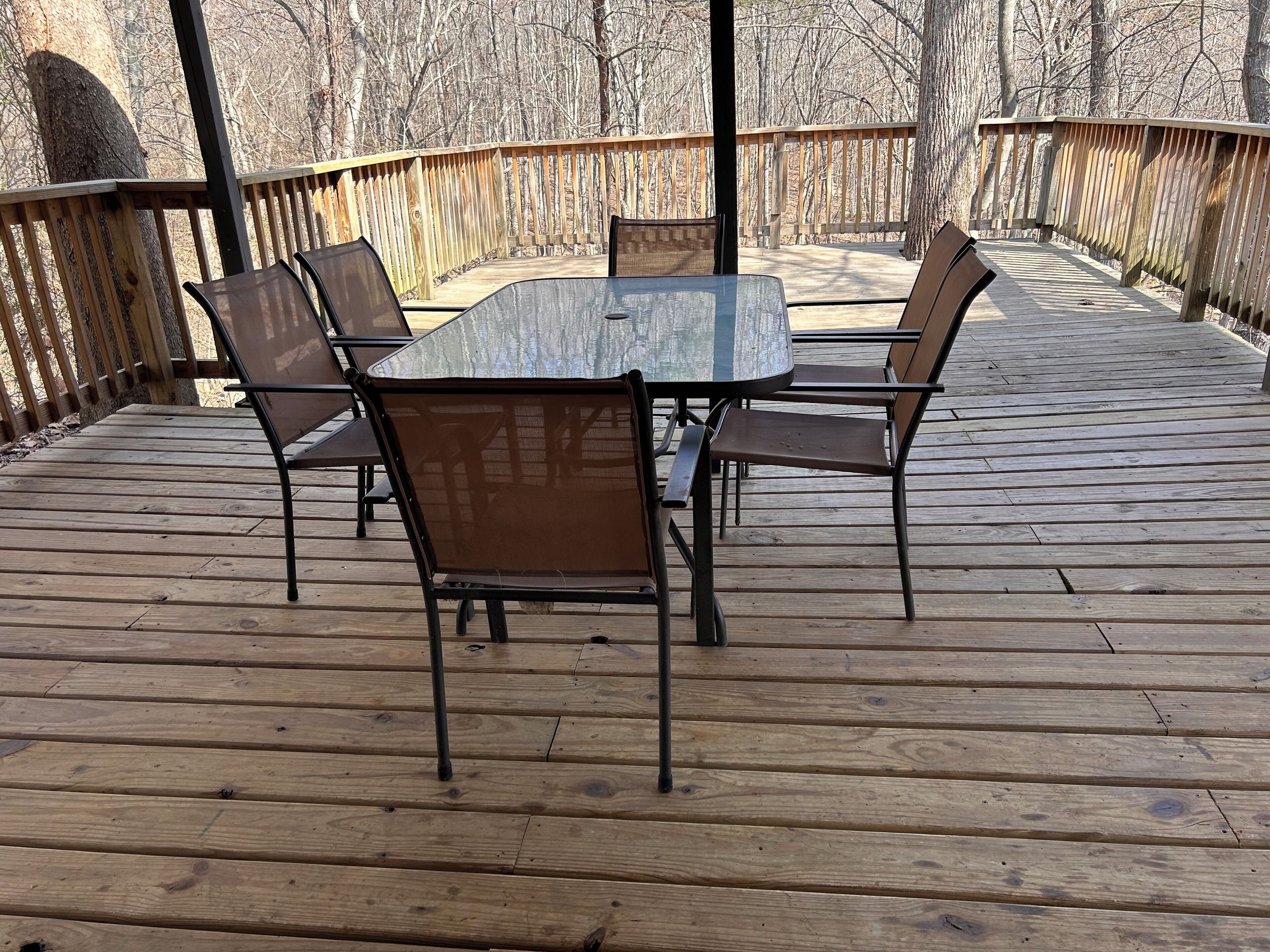 Una terraza de madera con una mesa y sillas, rodeada por un barandal de madera.