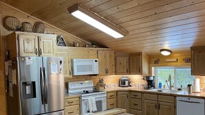 A modern kitchen with wooden cabinets, stainless steel appliances, and a large island. - Adventure Basecamp near YNP • Hot Tub + Toy Garage (Island Park)