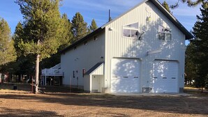 A white metal barn with a covered porch and two garage doors. - Adventure Basecamp near YNP • Hot Tub + Toy Garage (Island Park)