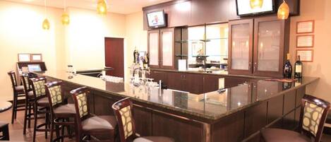 A bar area with a long counter, multiple bar stools, and a television mounted above the counter.