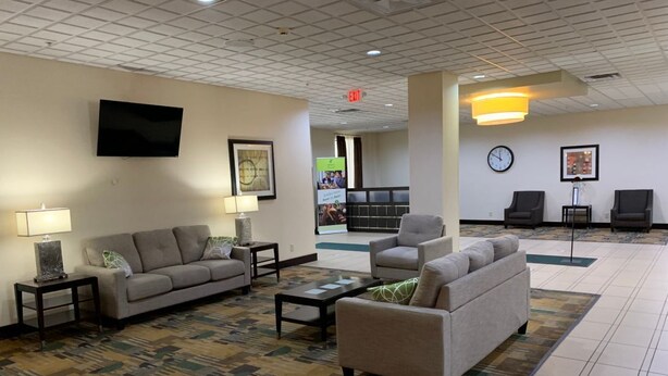 A hotel lobby with a sofa, armchairs, a coffee table, a TV, and a clock on the wall. - Quality Inn & Suites Downtown Mansfield (Mansfield)