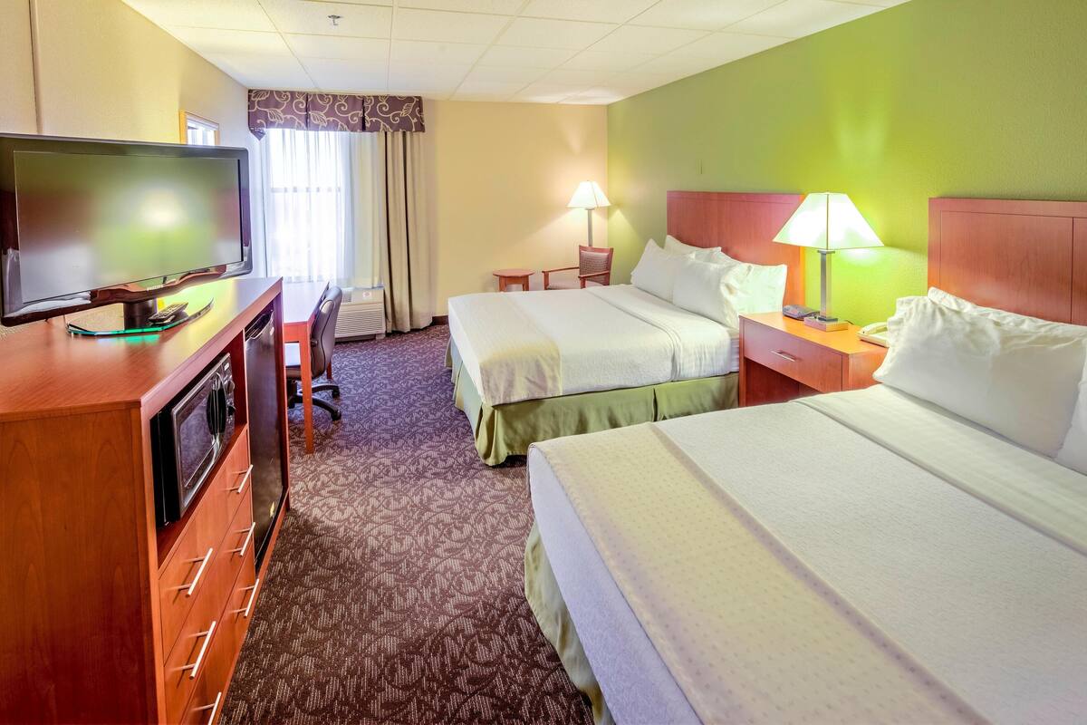 Ein Hotelzimmer mit zwei Betten, einem Schreibtisch, einem Flachbildfernseher, einer Lampe und einem Stuhl.