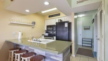 A compact kitchen with a central island, bar stools, a refrigerator, and a microwave.