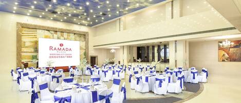 A spacious hall with rows of round tables, each with white tablecloths and blue sashes, set up for an event.