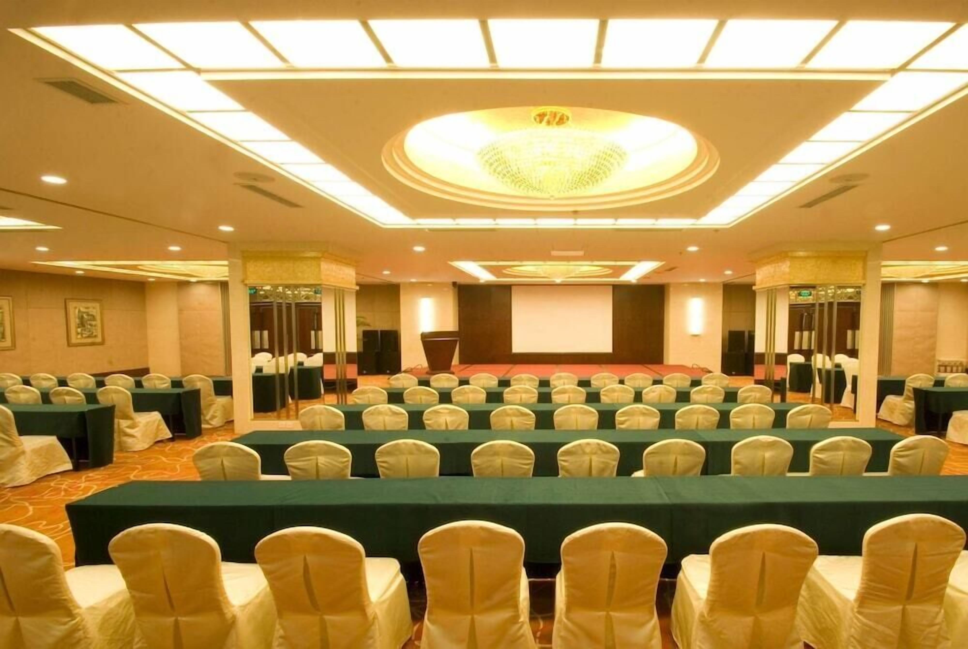 A conference room with rows of tables and chairs, a large screen, and a podium.